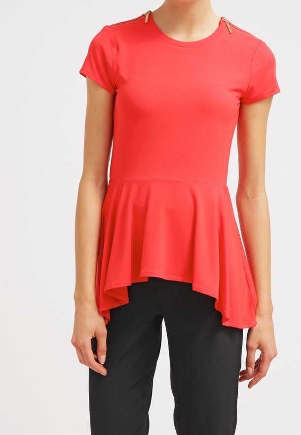 Röd peplumtopp med korta ärmar, med guldaccenter vid axelsömmarna och en flytande, asymmetrisk fåll. Slät tygtextur.