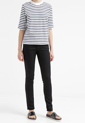 Wzorzysty T-shirt z krótkim rękawem w białym i granatowym kolorze, zestawiony z czarnymi, dopasowanymi dżinsami oraz czarnymi sandałami z teksturowanym paskiem i białą podeszwą.