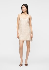Robe beige sans manches avec une texture transparente, ornée d'un motif de petits sequins, tombant au-dessus des genoux.