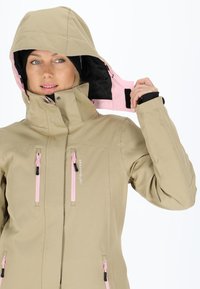 Giacca impermeabile beige con cerniere rosa e cappuccio. Presenta due tasche frontali e cappuccio regolabile. Realizzata in materiale resistente e liscio.