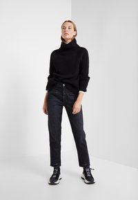 Black ribbed turtleneck sweater, dark denim jeans, and black athletic shoes. Simple design with a relaxed fit and minimal accents.