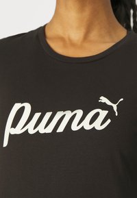Czarny t-shirt z białym napisem w stylu pisma "puma" oraz małą grafiką skaczącego pumy w górnym prawym rogu. Krótkie rękawy, okrągły dekolt.