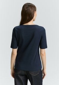 Marineblaue Kurzarm-T-Shirt mit rundem Halsausschnitt und glatter Textur, kombiniert mit dunklen Denim-Jeans, von hinten betrachtet.