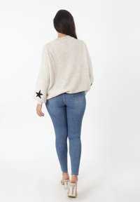 Maglione lavorato a maglia avorio con una vestibilità morbida, caratterizzato da accenti neri a forma di stella sulle maniche. Abbinato a jeans blu aderenti e sandali trasparenti con tacco a blocco.