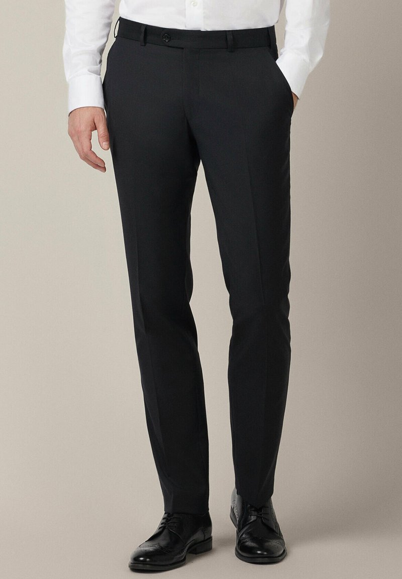 Czarne eleganckie spodnie wykonane z gładkiego materiału, o dopasowanym kroju, z pętelkami na pasek i dwiema bocznymi kieszeniami, w połączeniu z czarnymi butami.