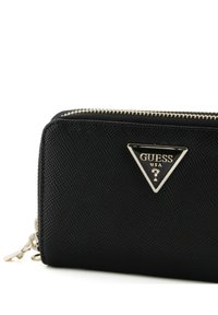 Portafoglio nero con texture, dotato di zip argentata e di una placca a logo triangolare con la scritta "GUESS USA." Esterno liscio con decorazioni minime.