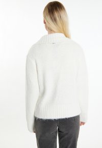 Pullover bianco accogliente in morbido materiale peloso, caratterizzato da un orlo a coste ampio e un colletto ripiegato. La vista posteriore non mostra ulteriori motivi o accenti.