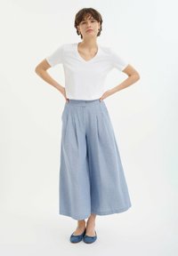 Lichtblauwe wijde broek met hoge taille en plooien, gecombineerd met een witte T-shirt met korte mouwen en V-hals en blauwe balletschoenen.