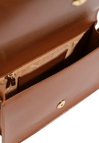 Borsa a mano in pelle marrone con una texture liscia, dotata di una tasca con zip e un chiusura a scatto in metallo dorato. La fodera interna è chiara.