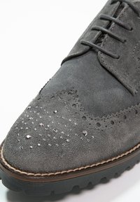 Chaussure habillée en suede gris avec des détails de brogue, une texture lisse, des accents scintillants et une semelle en caoutchouc contrastée avec un léger talon.