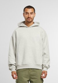 Lichtgrijze hoodie met een kangoeroezak, ribgebreide manchetten en zoom. Bevat een subtiele geborduurde logo op de borst. Zachte, textuurstof.