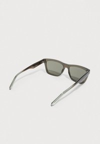 Brązowe okulary przeciwsłoneczne o kwadratowym kształcie, z przezroczystymi szarymi zausznikami i ciemnoszarymi soczewkami. Elegancki, minimalistyczny design bez widocznych logo.