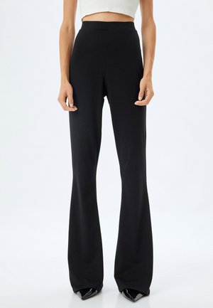Pantalones acampanados negros de tela elástica, con una cinturilla alta y un diseño elegante, que llegan hasta el suelo, combinados con tacones de punta.