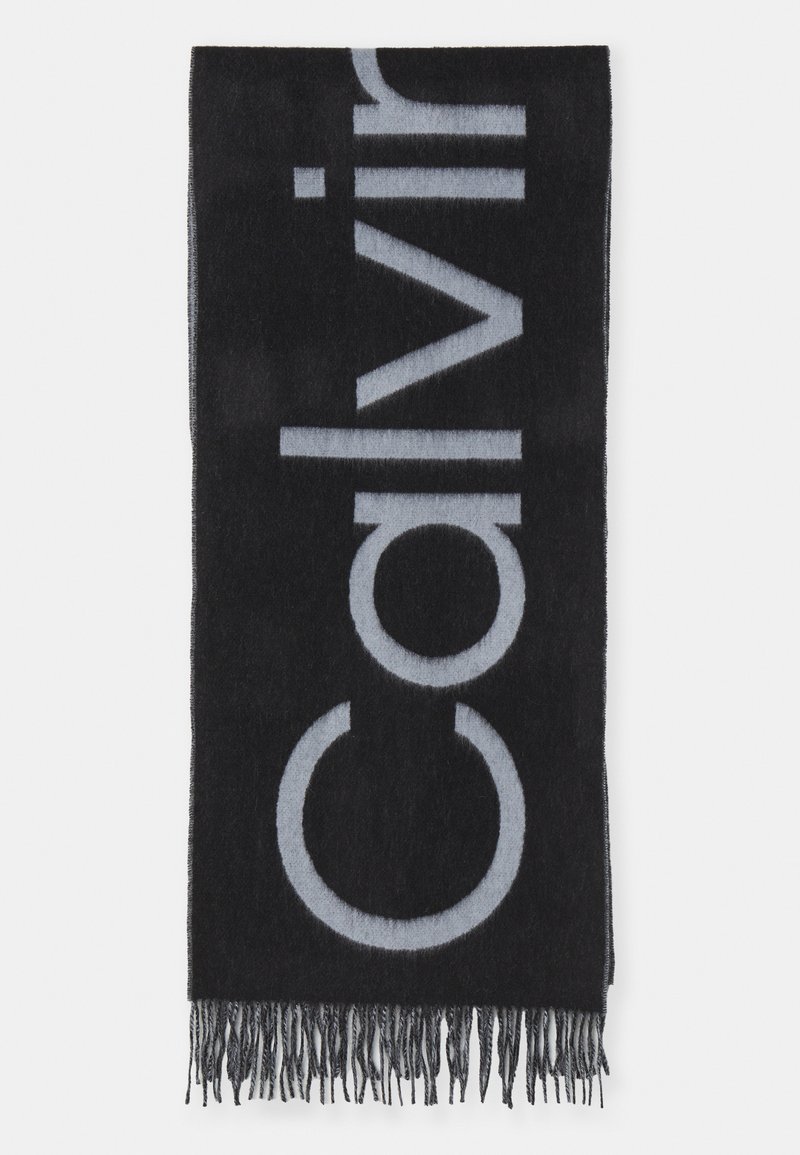 Juodas šalikas su dideliu pilku tekstu, minkšta tekstūra ir plonu kraštu. Medžiaga atrodo kaip vilna arba panaši tekstilė.