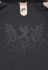 Schwarzer Stoff mit einem grauen grafischen Design, das ein Schild, einen Cherub, Flügel und den Text "Gipry" sowie "INTERNATIONAL FASHION" zeigt, mit strukturierter Oberfläche.