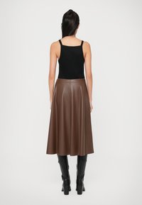 Brown faux leather midi skirt, flared design, smooth texture, paired with a black fitted tank top and knee-high black boots.