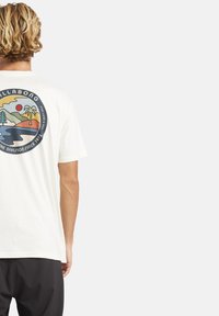 Weißes Baumwoll-T-Shirt mit einem runden Grafikdruck auf der Rückseite, der eine Landschaft mit Bäumen, Wasser und einer Sonne in sanften Pastellfarben darstellt.