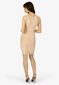 Knee-length, figurnära klänning i ljusbeige med horisontell ribbad struktur och en central dragkedja bak. Kombineras med klara sandaletter med blockklack.