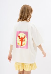 Witte oversized t-shirt met een kreeftgraphic in het rood op een gele achtergrond met roze strepen. Van zacht katoen, relaxte pasvorm.