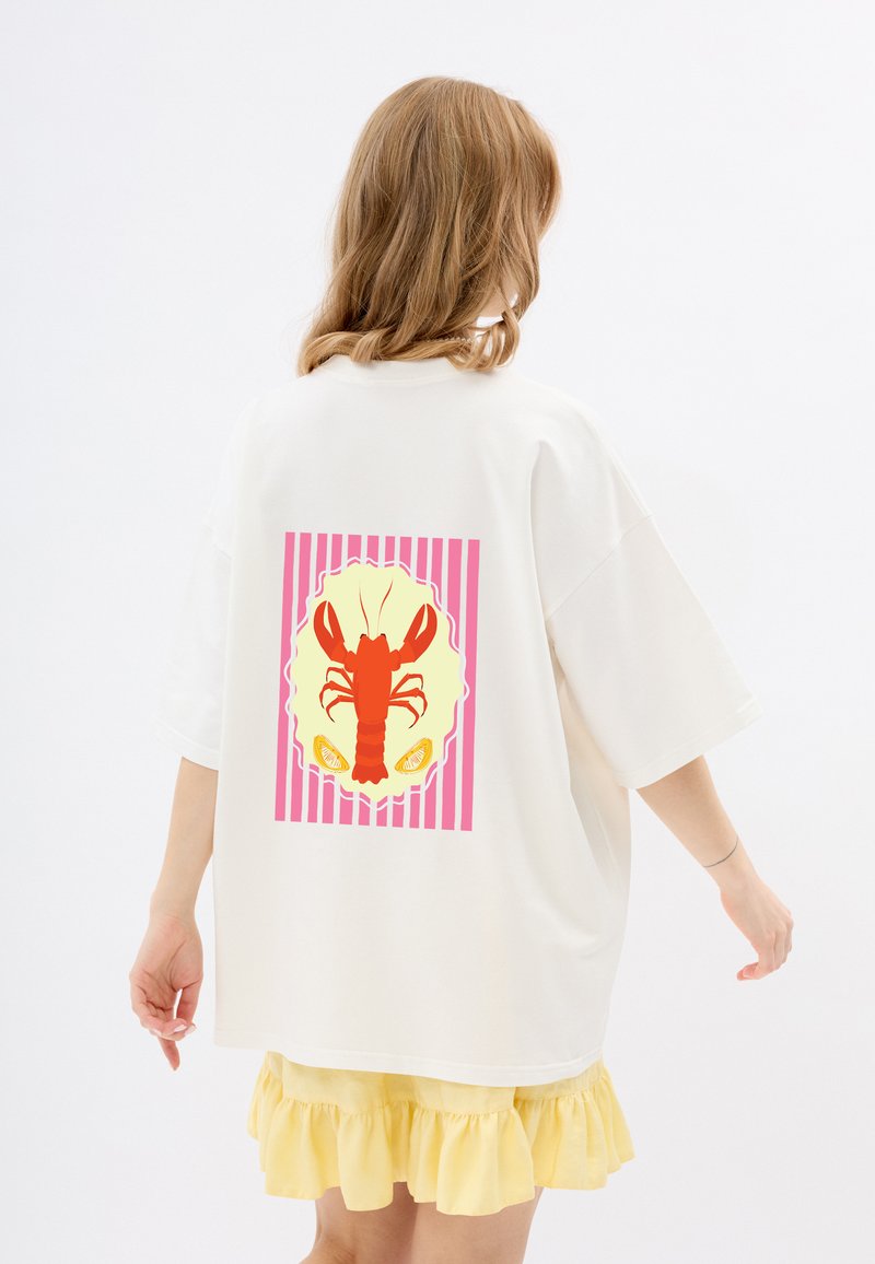 Witte oversized t-shirt met een kreeftgraphic in het rood op een gele achtergrond met roze strepen. Van zacht katoen, relaxte pasvorm.