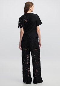 Camiseta de jersey negra con espalda de encaje y patrones florales. Combinada con pantalones anchos de encaje negro, texturizados con diseños recortados.