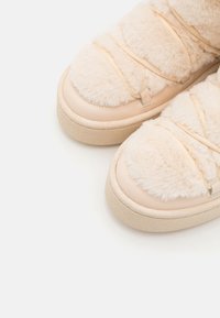 Beige fôrdet sko med glatte lærdetaljer, avrundet form og elastiske stropper. Teksturert såle gir grep og støtte.