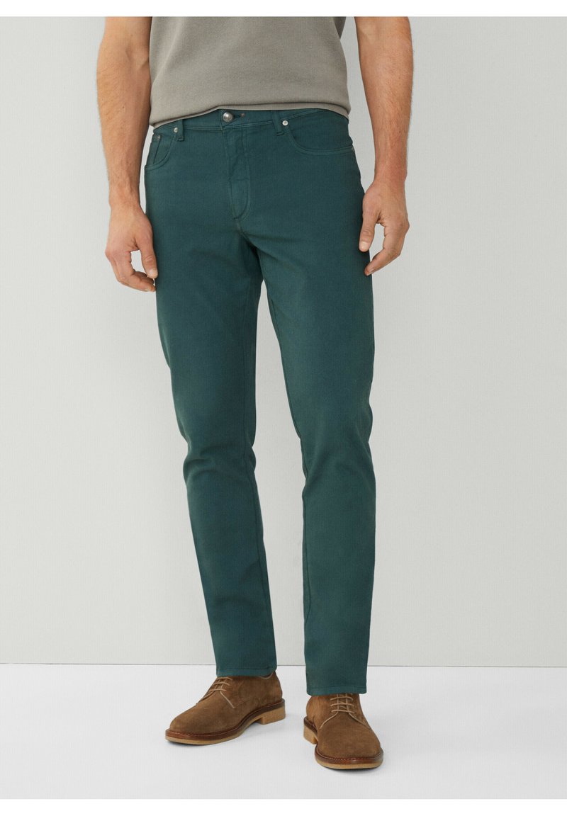 Groene katoenen broek met een slim-fit ontwerp, voorzien van vijf zakken en een knopenfly. Draagt met bruine suède schoenen.