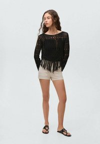 Zwarte gehaakte top met een open geweven ontwerp en franjes, gecombineerd met beige shorts en zwarte sandalen. Gladde textuur, casual pasvorm.