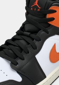 Schwarz-weiße High-Top-Sneaker mit orangen Akzenten, strukturiertem Leder, flachen schwarzen Schnürsenkeln und einem genähten Design mit durchbrochenen Details.