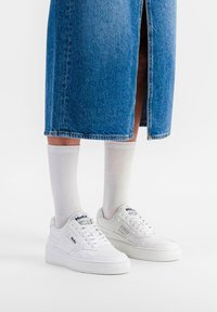Hvite sneakers med en teksturert overflate, med logo og perforeringer, sammen med knelange hvite sokker og et denimskjørt.