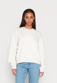 Sweatshirt bege claro com decote redondo, apresentando um gráfico texturizado branco de "amor" na parte da frente. Concebido com mangas e barra largas.