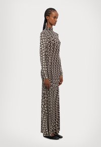 Robe à manches longues, avec un motif zigzag noir et blanc, un col haut, une silhouette ajustée et un tissu lisse, accompagnée de chaussures plates noires.