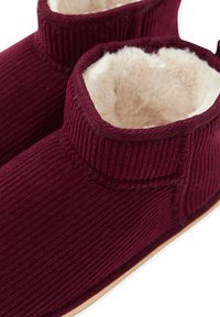 Burgundowe kapcie z weluru z miękkim, kremowym futerkiem w środku, z wysokim kołnierzem i minimalistycznym wzornictwem. Gładka gumowa podeszwa.