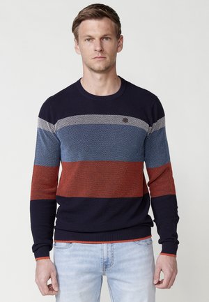 Jersey de cuello redondo a rayas en azul marino, rojo y azul, con punto texturizado, puños y dobladillo acanalados, exhibido en un modelo sobre un fondo neutro.