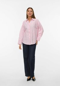 Camicia a righe rosa con maniche ampie, caratterizzata da sottili righe verdi e bianche. Abbinata a jeans dritti blu scuro.
