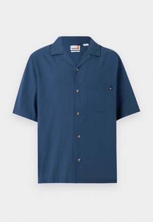 Chemise bleu marine à manches courtes avec boutons, poche poitrine et col à revers, présentée sur un fond clair uni.