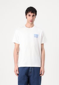 White cotton T-shirt with short sleeves, featuring blue text "STANCE AUTOMOTIVE UPHOLSTERY" on the left chest area. Classic fit.