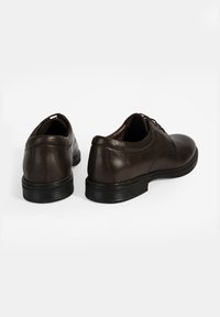 Braune Lederschuhe mit glatter Oberfläche, runder Zehenform und niedriger schwarzer Gummisohle. Mit Schnürsenkeln und dezenten Nahtdetails an den Seiten.
