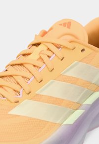 Primo piano di una sneaker Adidas arancione con lacci, strisce bianche sul lato e suola viola.