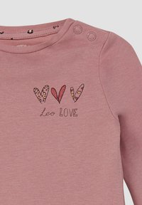 Langärmliges pinkes Oberteil mit rundem Ausschnitt, verziert mit drei Herzen in verschiedenen Mustern und dem Text "Leo LIEBE" darunter. Druckknöpfe an der Schulter.