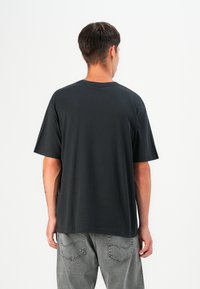 Black cotton t-shirt with short sleeves, round neckline, and relaxed fit, displayed from the back with gray denim pants.