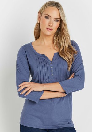 Maglietta blu a maniche lunghe con scollatura a V, patta di bottoni e texture plissettata sulla parte anteriore per un tocco di dettaglio. Tessuto morbido.