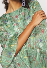 Abito floreale verde con un design a pieghe tessurizzato. Caratterizzato da maniche lunghe fino al gomito e una vita arricciata, decorato con fiori multicolori.