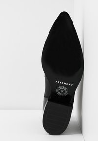 Chaussure noire à talons hauts avec un bout pointu, une semelle texturée et un marquage discret. Le talon mesure environ 8 cm de hauteur.