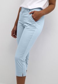 Light blue cropped pants made of soft fabric, featuring side pockets and a split at the hem for added detail.