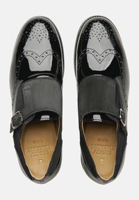 Schwarze Lacklederschuhe mit Brogue-Details, elastischem Einsatz und Schnallenakzent. Sie zeichnen sich durch eine glatte Textur und ein rundes Design der Zehenpartie aus.