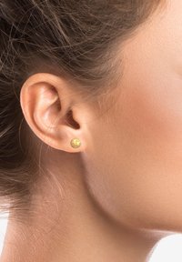 Boucles d'oreilles en or avec un design de star en relief, présentant une surface lisse et une forme ronde, mises en valeur dans l'oreille d'un modèle.