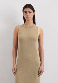 Robe sans manches en tricot de couleur beige avec un col rond à côtes. Texture douce et silhouette ajustée, atteignant la longueur mi-mollet.