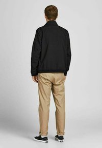 Sort bomberjakke med ståkrave, kombineret med khakifarvede chinos og sorte sneakers. Glat tekstur, elastiske manchetter ved ærmer og talje.