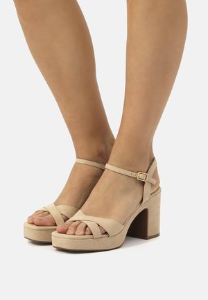 Sandales plateformes en suède beige avec design à croix, boucle à la cheville et talon épais. Matériau texturé, bout ouvert.